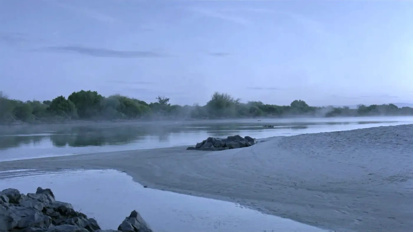 The Zambezi riverbank at first light, clean sand and mist over the water